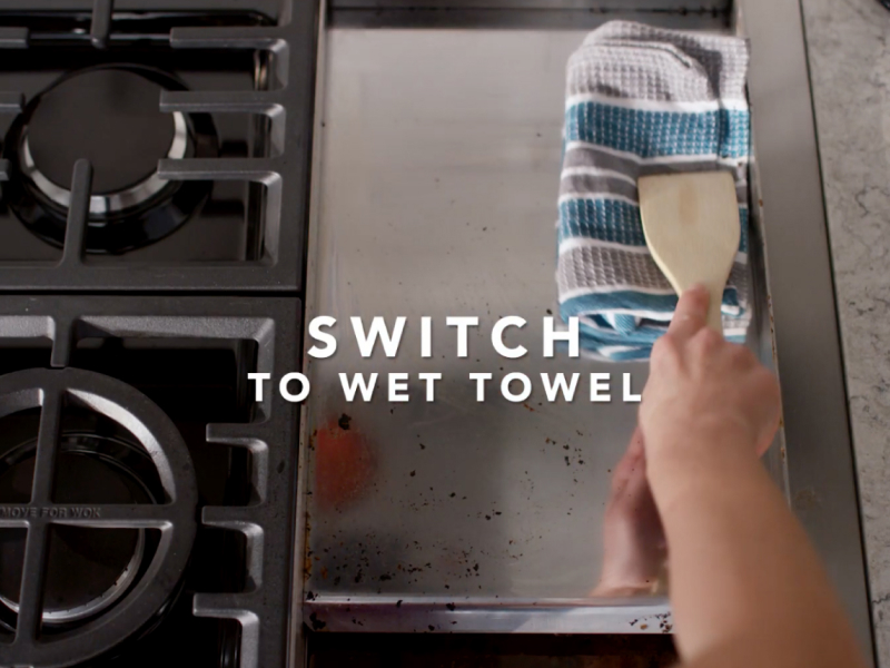 Wiping griddle clean with towel and wooden spoon 