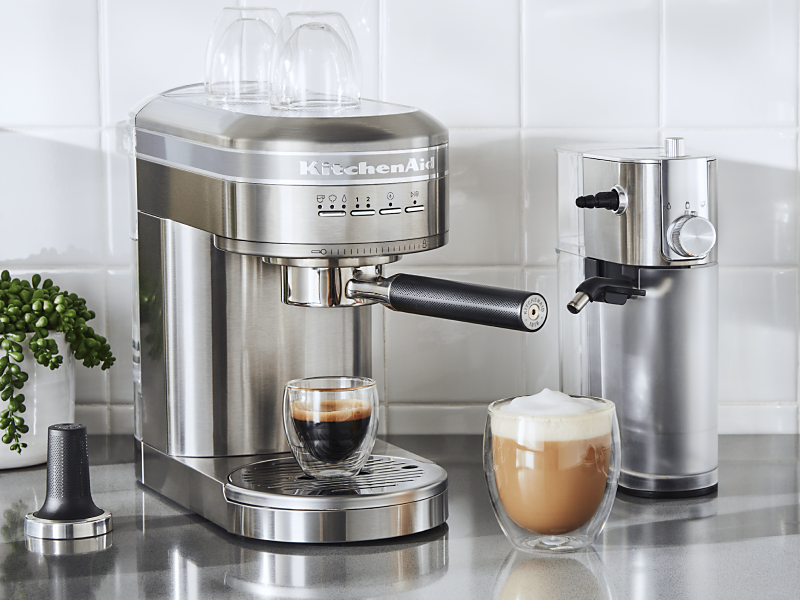 Espresso in a silver KitchenAid® Espresso Machine next to Automatic Milk Frother Attachment