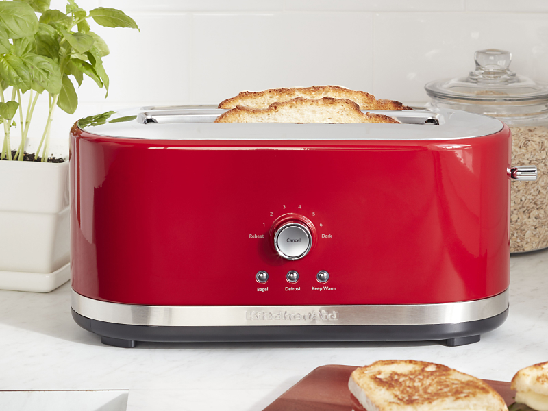 Slices of bread in a red KitchenAid® toaster on a modern kitchen counter.