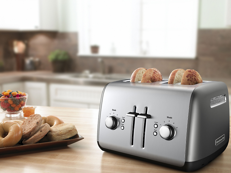 Bagel slices in a silver 4-slice KitchenAid® toaster on a modern kitchen counter.