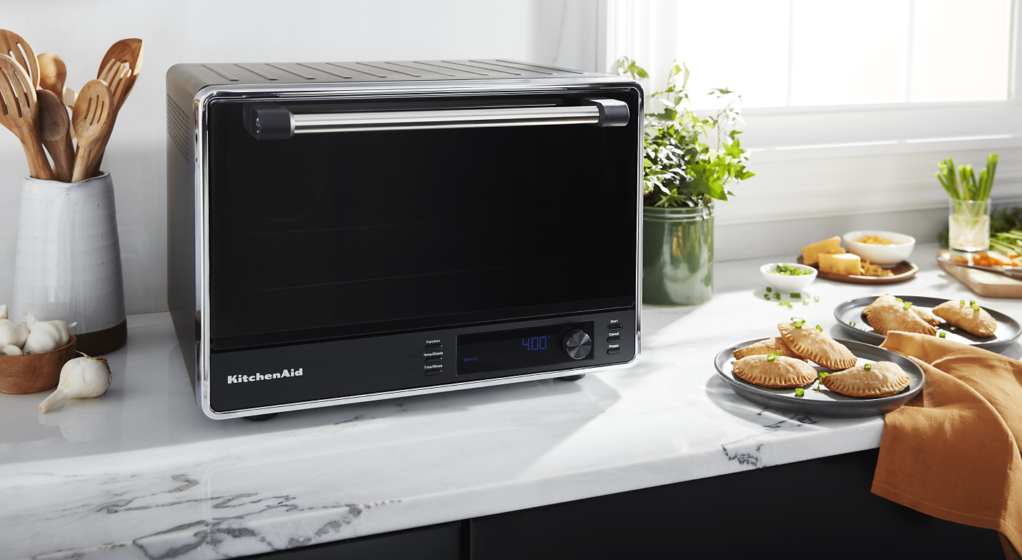 A black KitchenAid® air fryer and fresh empanadas on a countertop