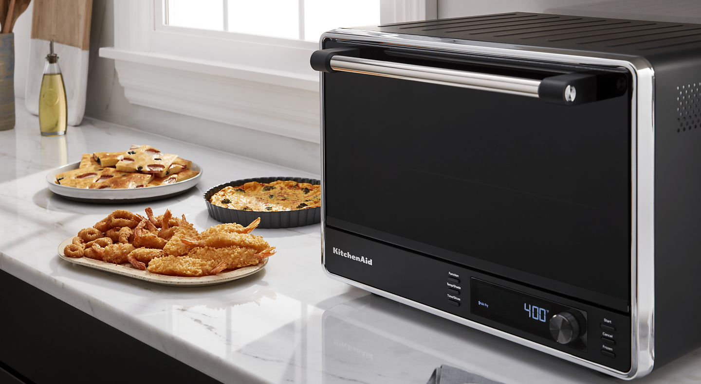 A black KitchenAid® air fryer and various appetizers on a countertop