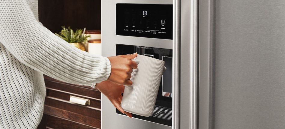 A woman filling a pitcher with water from the refrigerator door