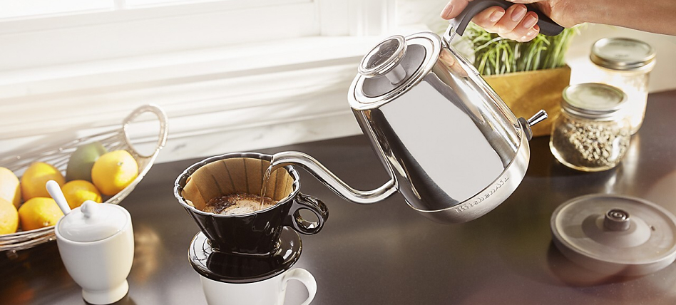A person pouring hot water from a kettle into a pour over cone A person pouring hot water from a kettle into a pour over cone