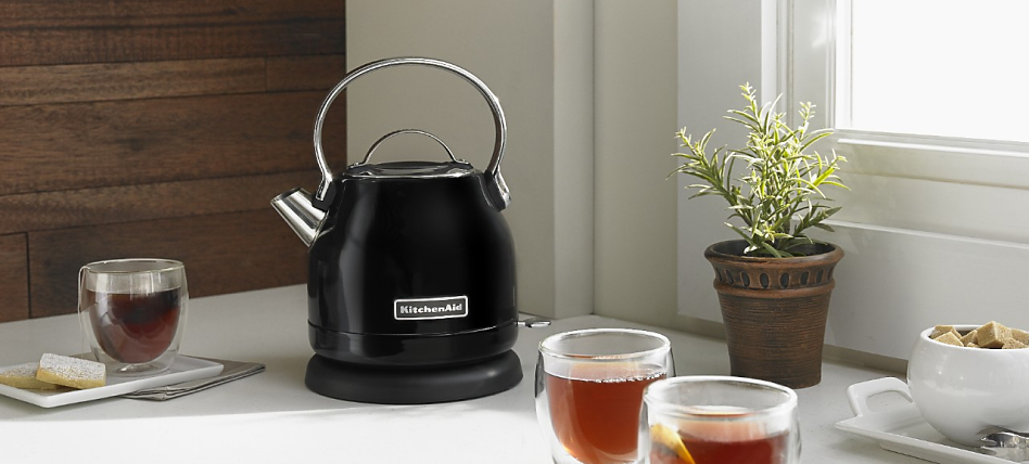 Black electric tea kettle on a countertop next to full glasses of tea