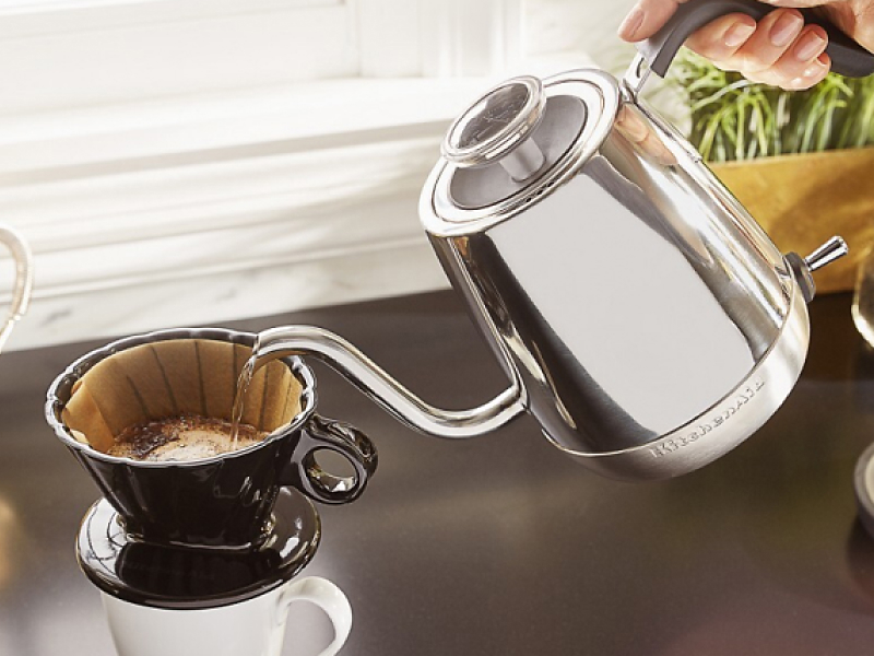 A woman pouring hot water from a KitchenAid® electric kettle into a pour-over coffee  mug