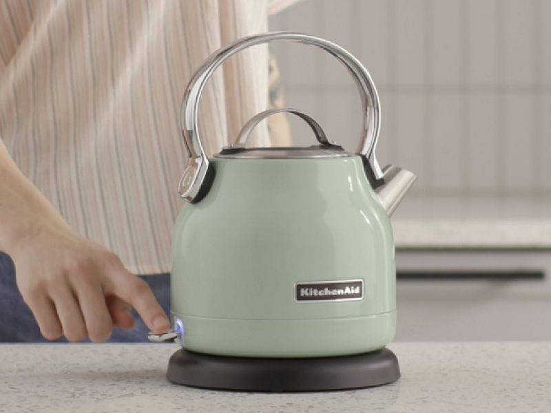 A woman using a KitchenAid® electric kettle in a modern kitchen