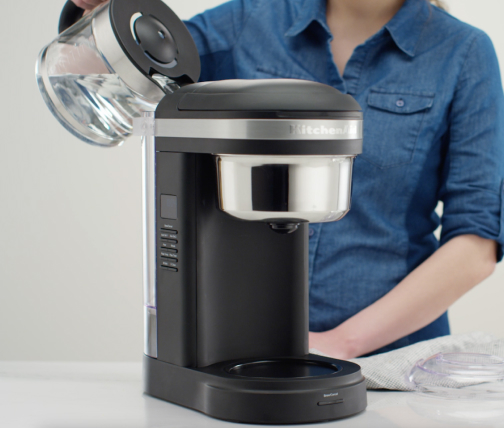 Woman pouring water into coffee machine to rinse after descaling