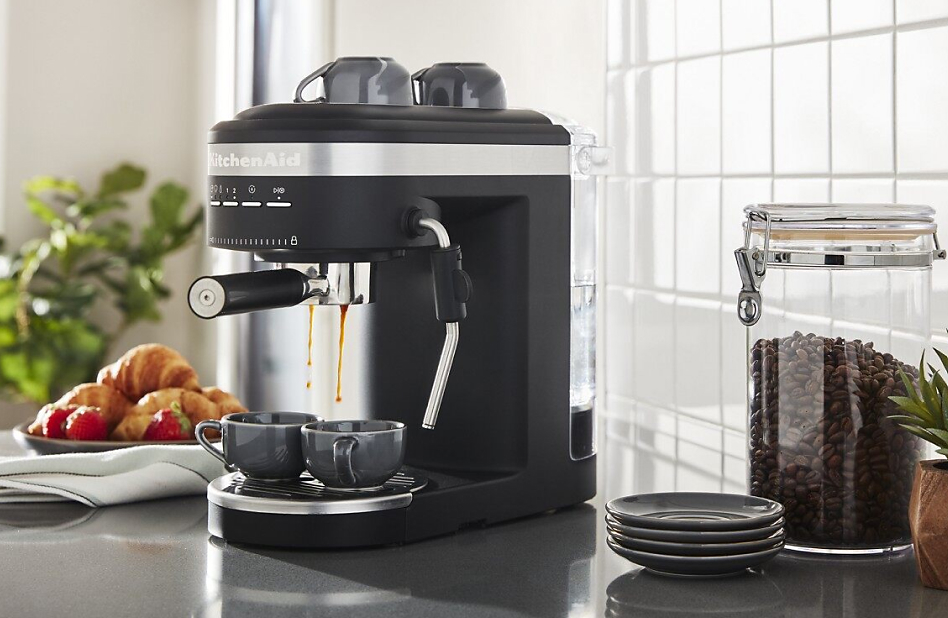 KitchenAid® espresso machine on countertop next to canister of coffee beans.
