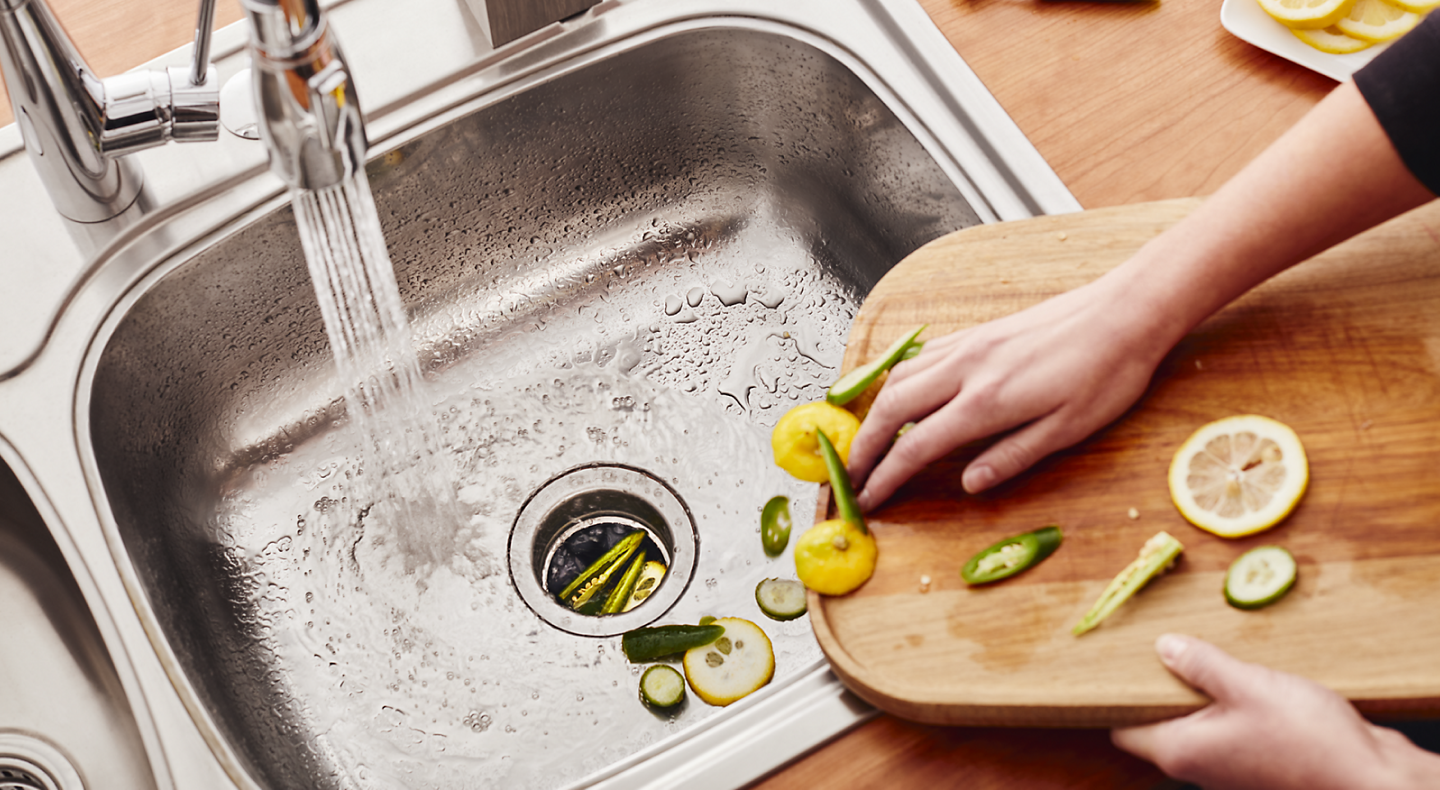 Person scraping vegetable scraps into a stainless steel sink