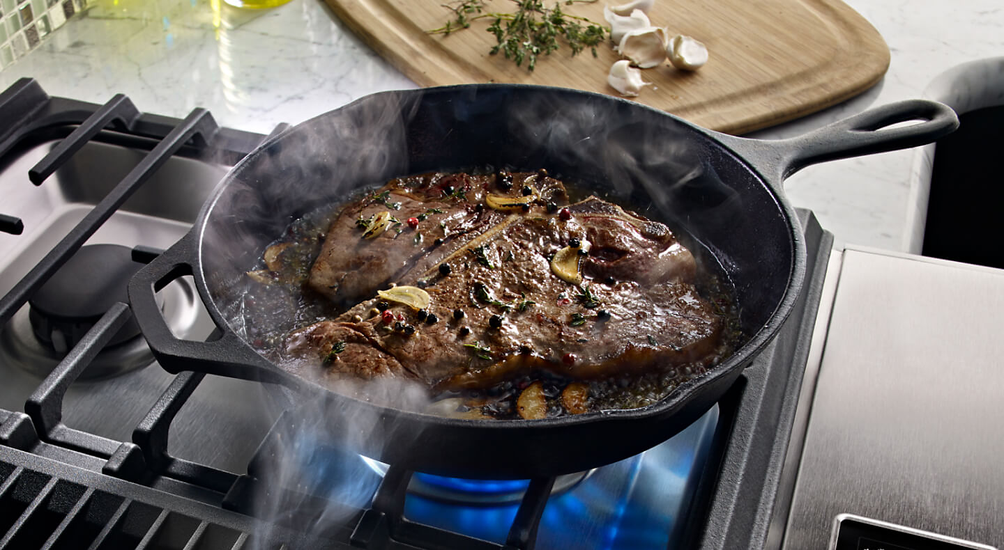 Steak cooking in a cast iron skillet in a kitchen with granite countertops.