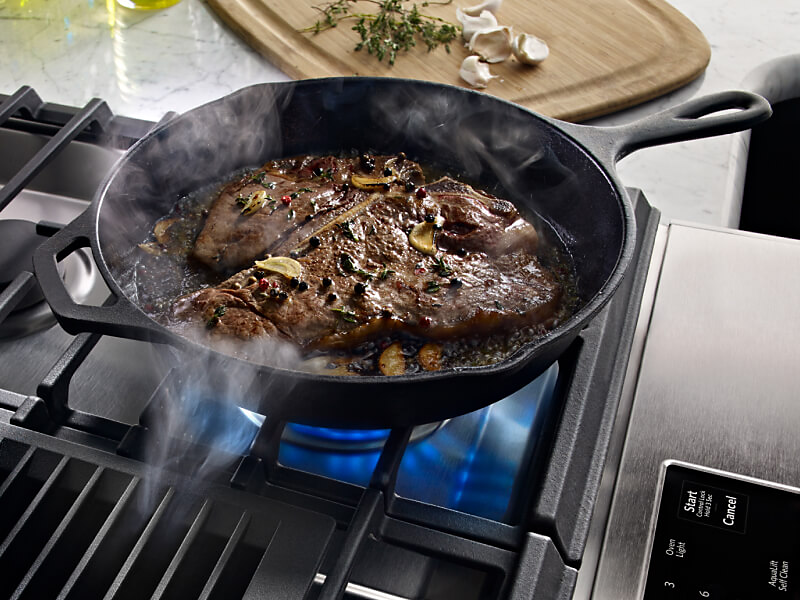 Steak cooking in a cast iron skillet in a kitchen with granite countertops.