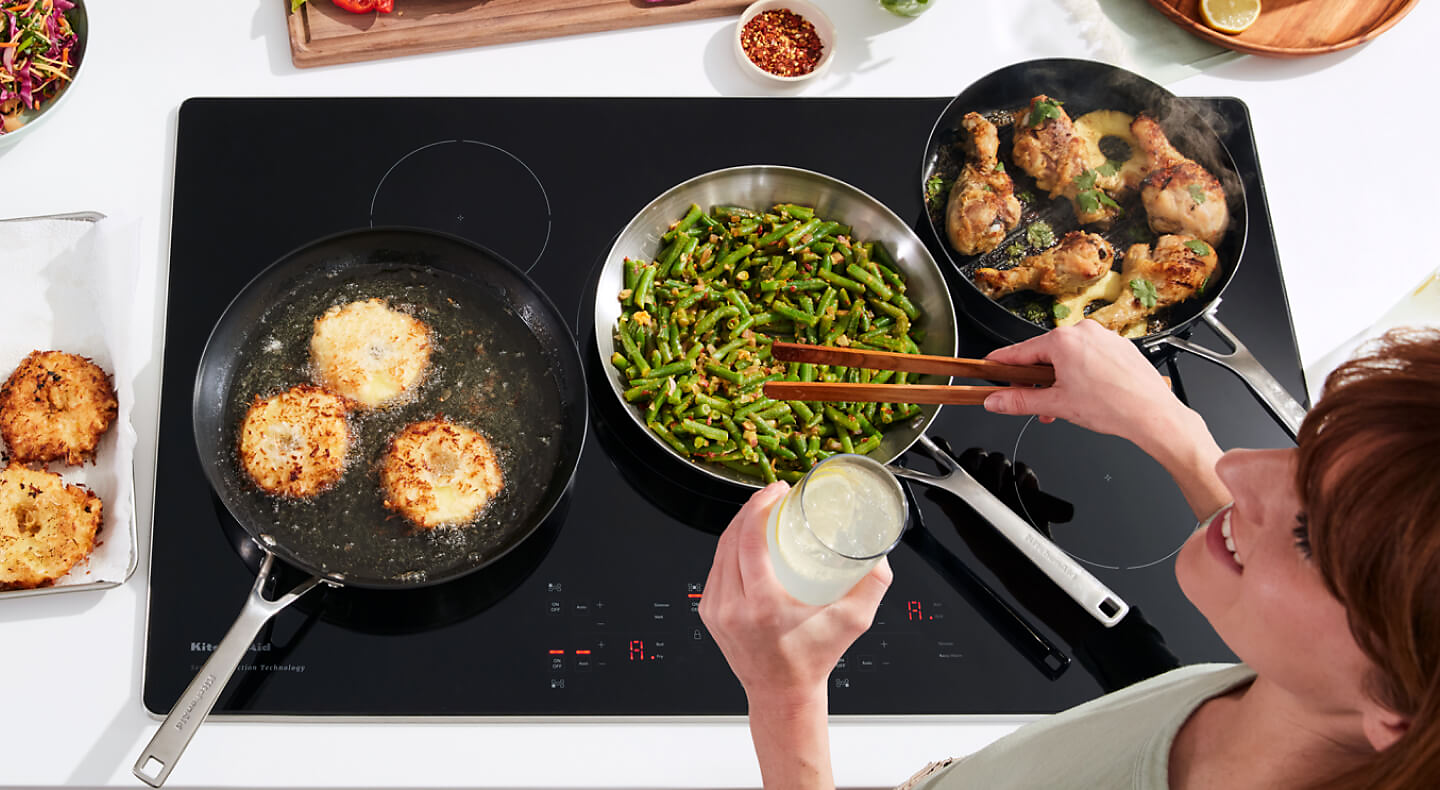 Person cooking chicken, green beans, and biscuits on an induction cooktop