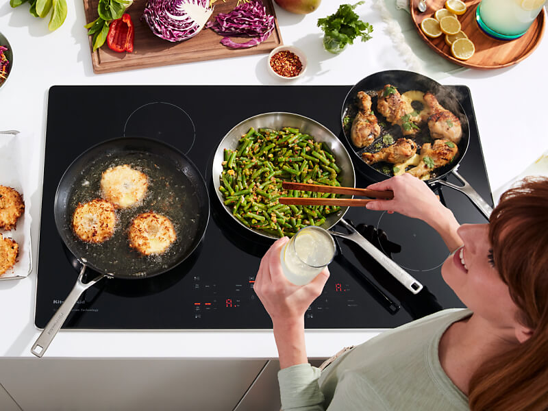 Person cooking chicken, green beans, and biscuits on an induction cooktop