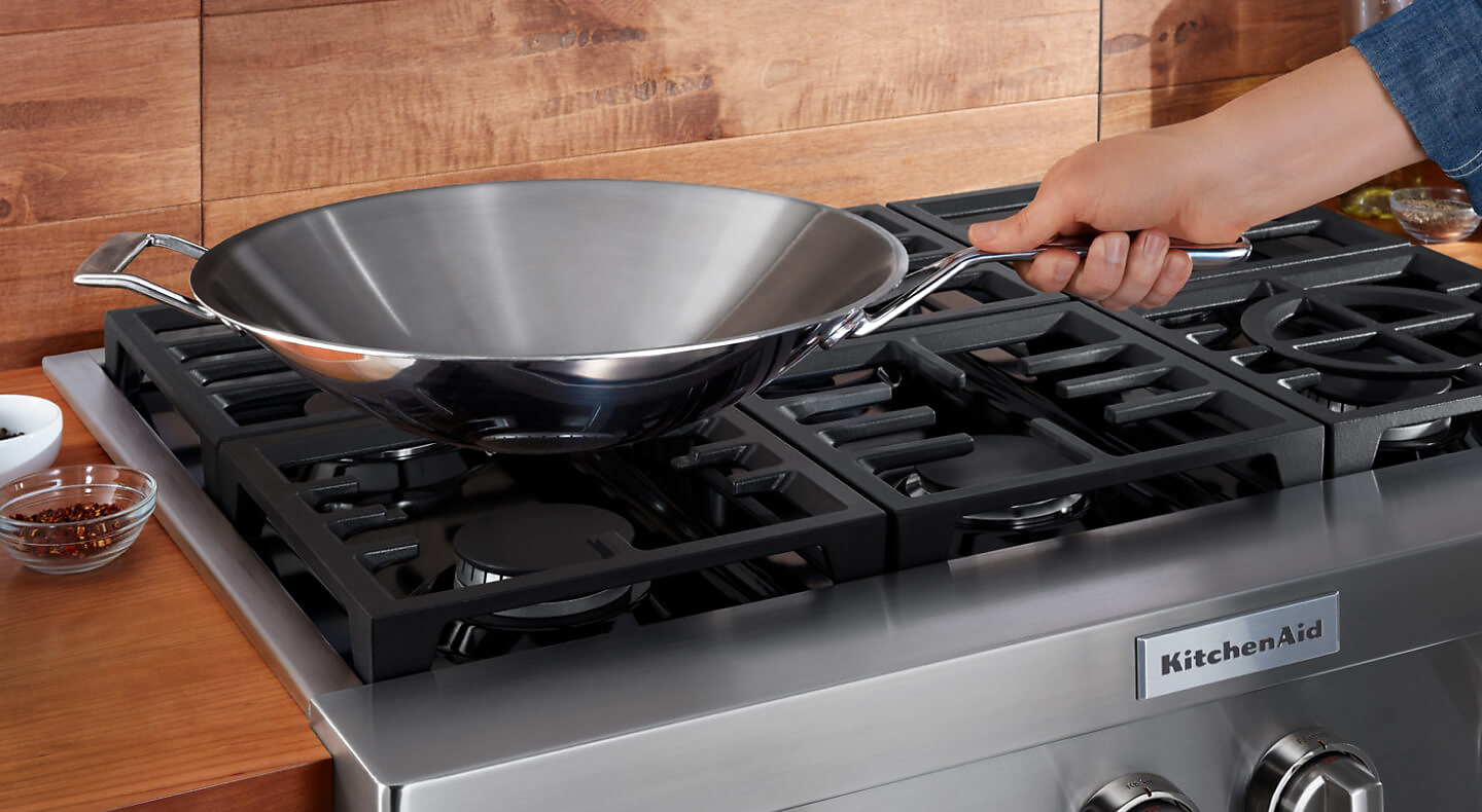Person holding a wok over a KitchenAid® brand gas range