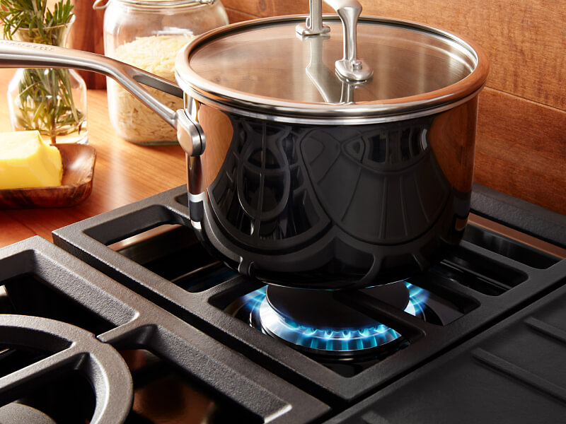 Pot cooking over a gas range against a wooden backsplash. 