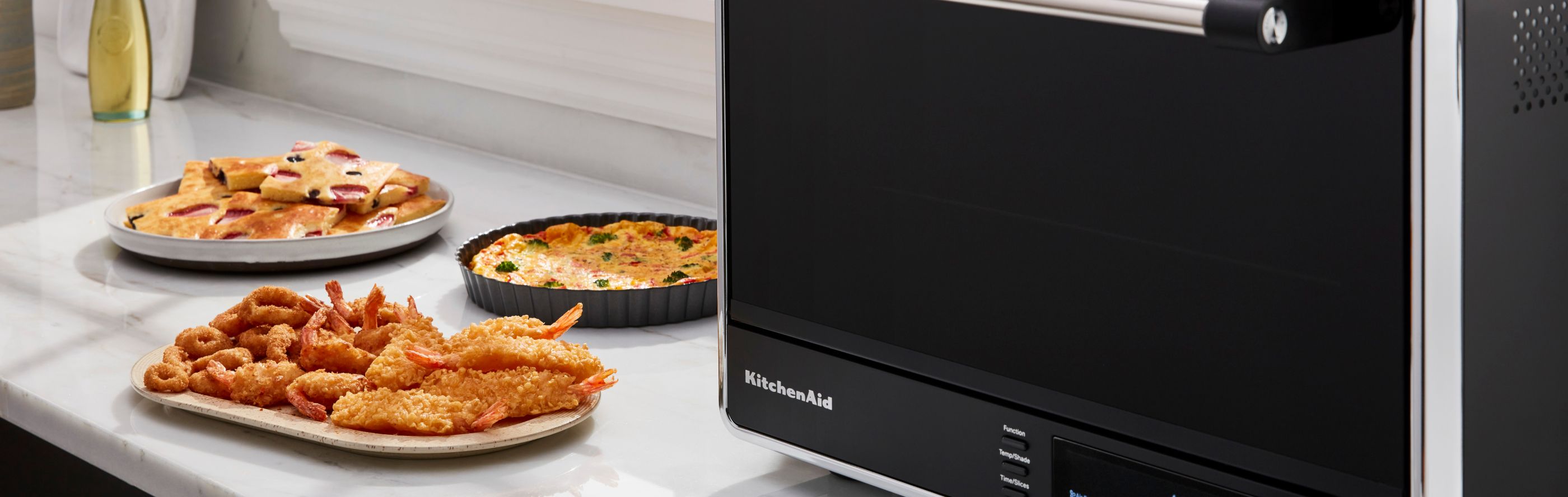 A KitchenAid® countertop oven with air fry on a modern kitchen counter next to air fried appetizers.