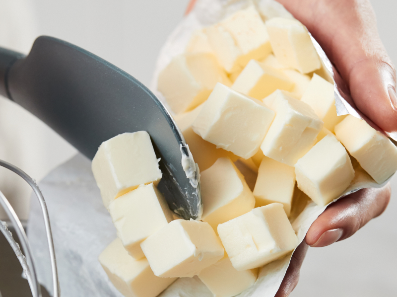Person spooning cubed butter into a mixer bowl