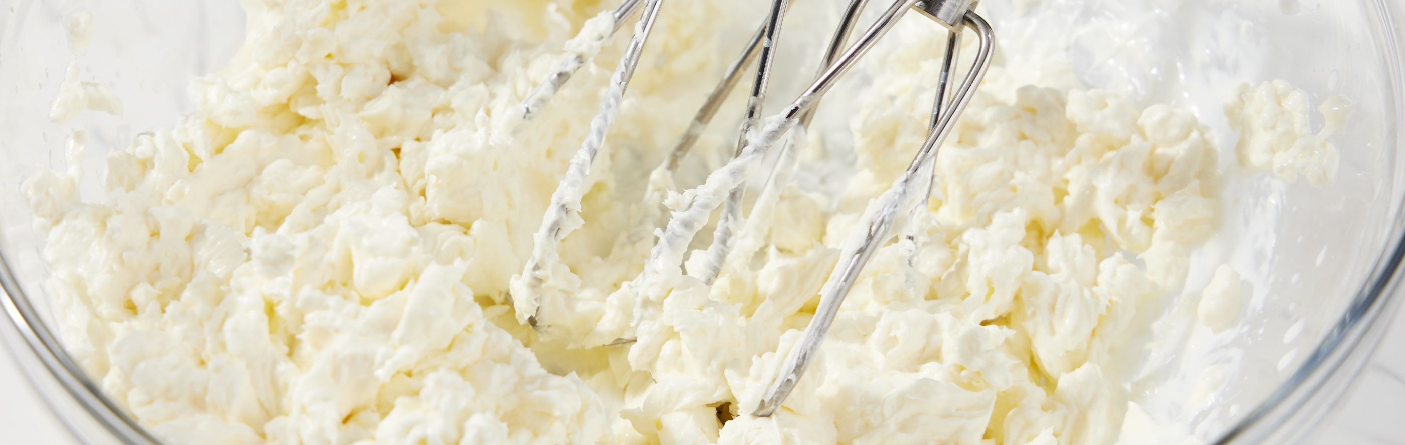 Hand mixer beaters in glass mixing bowl of creamed butter and sugar