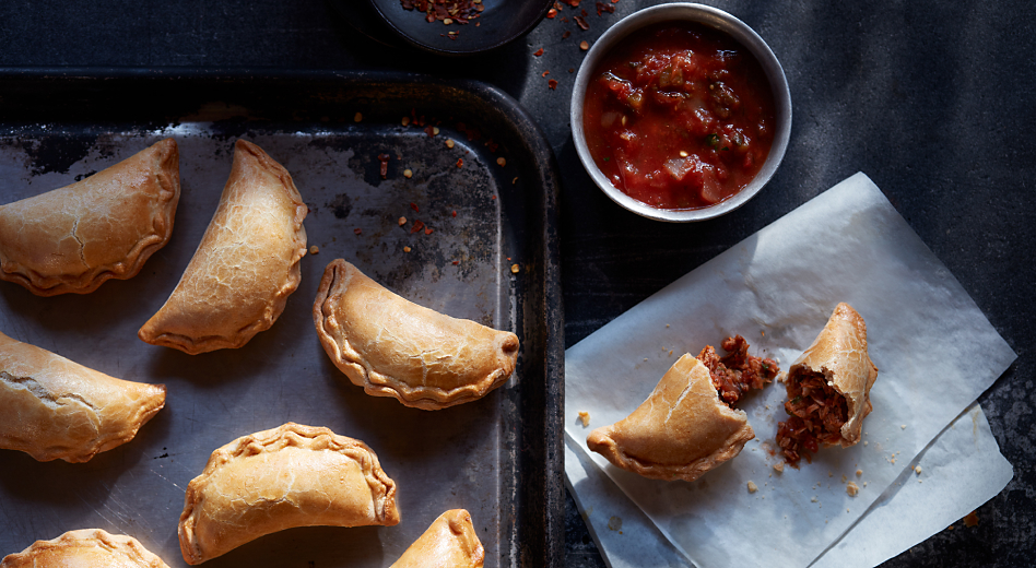 Empanadas on baking pan and on countertop with salsa