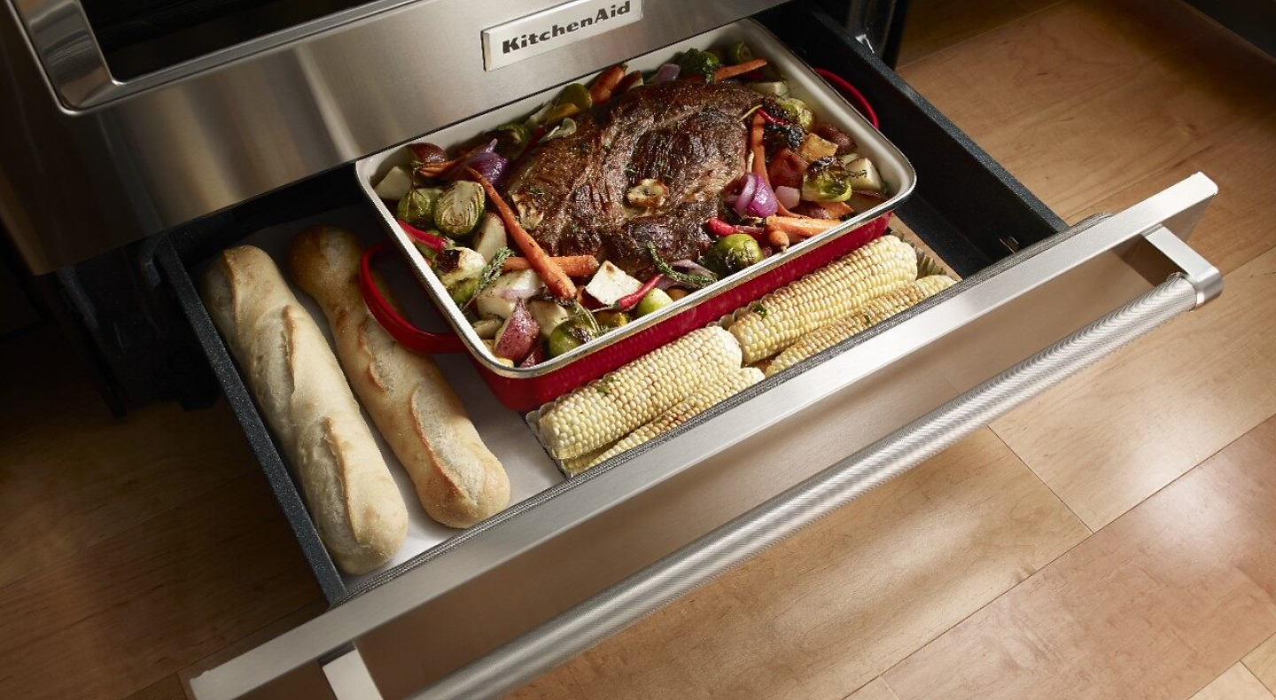 Open warming drawer with bread, a roast and vegetables inside