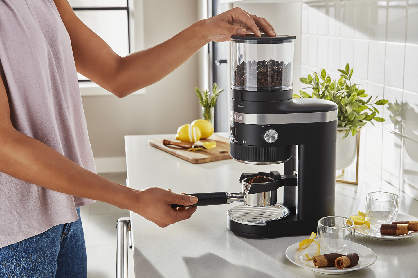 Woman removing portafilter with fresh coffee from KitchenAid® Burr Coffee Grinder