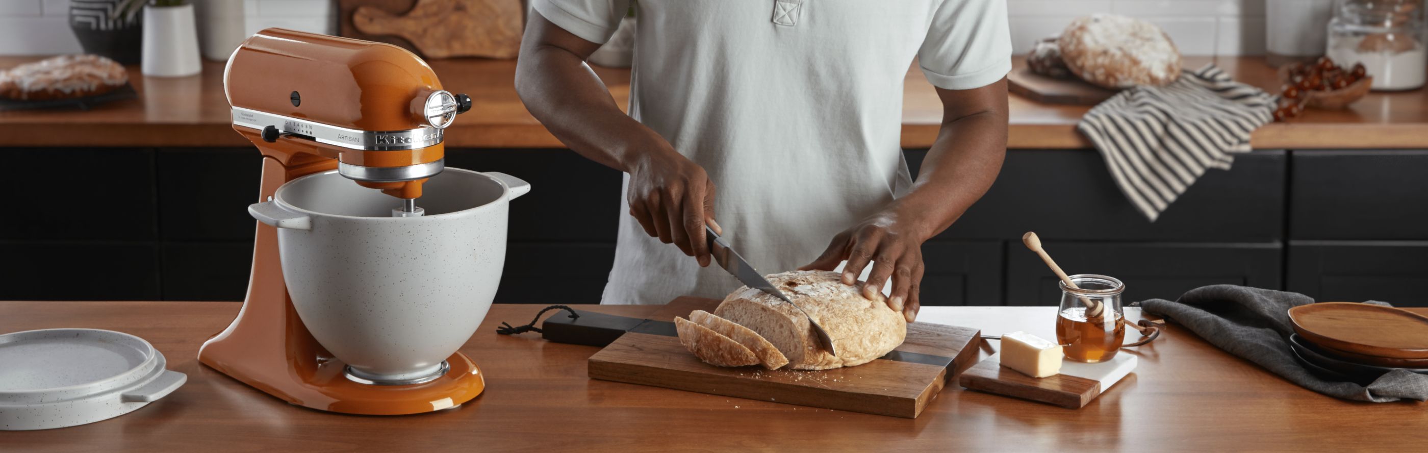 Man slicing fresh bread on countertop next to stand mixer