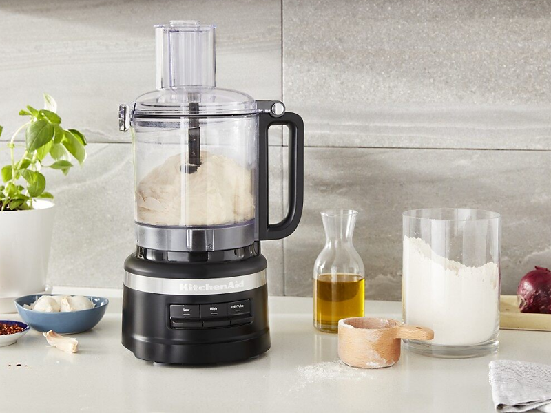 Food processor with dough inside and ingredients on countertop
