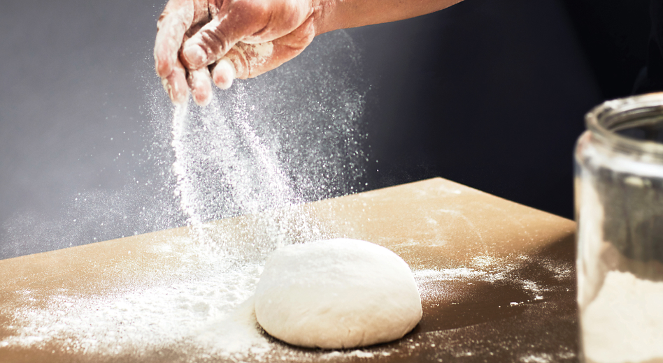 Hand sprinkling flour on ball of dough