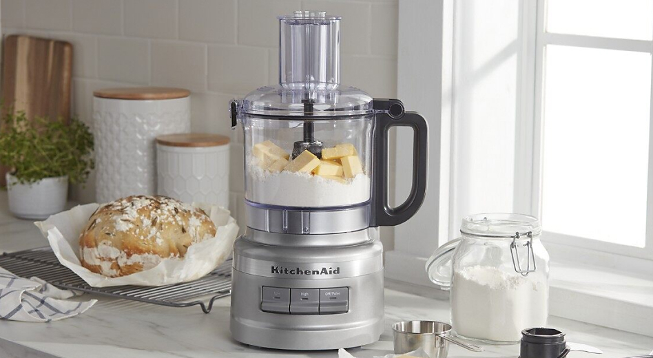 Stainless steel KitchenAid® Food Processor filled with cubes of butter and flour sitting on countertop next to loaf of bread and glass jar of flour