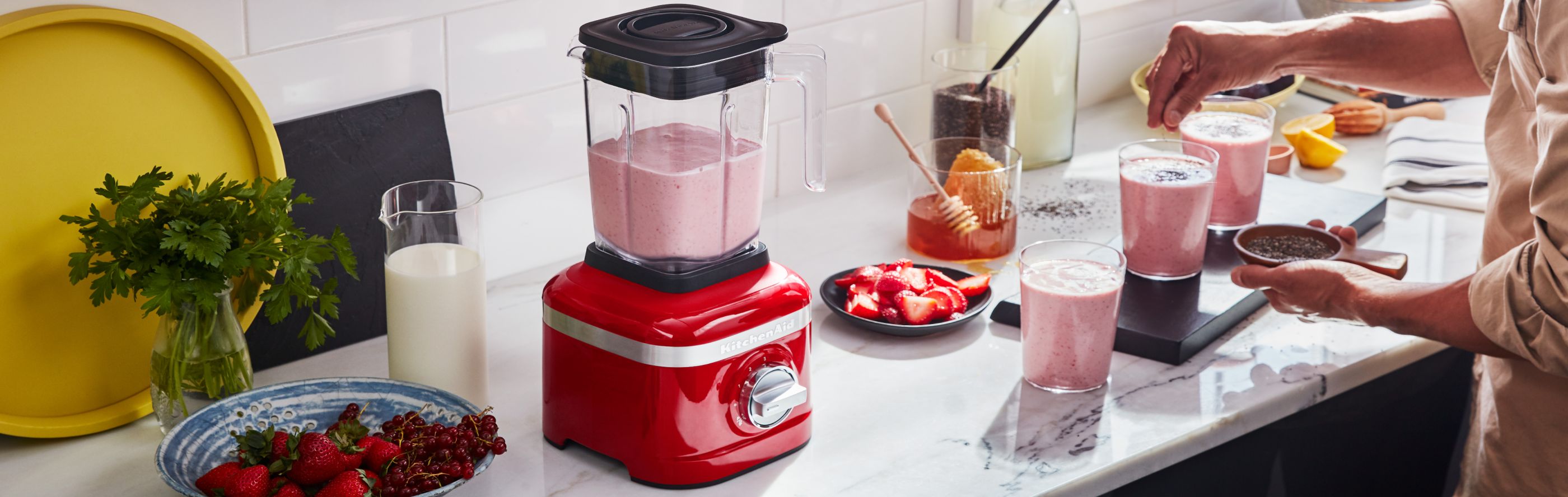 Person preparing strawberry milkshakes with a red blender