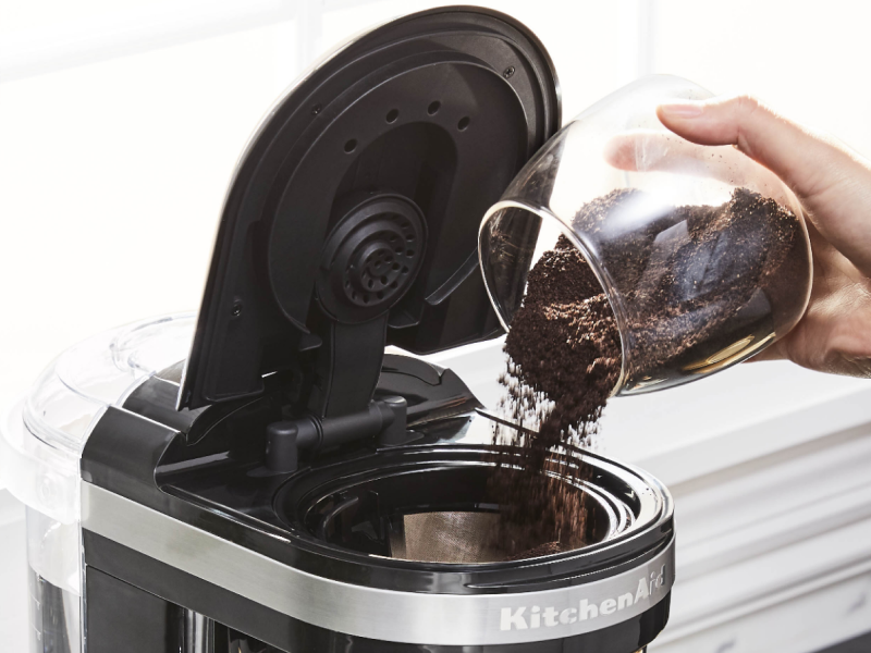 Person pouring coffee grounds into a KitchenAid® coffee maker