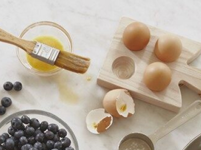 Ingredients including eggs next to egg wash and  beside a bowl of blueberries