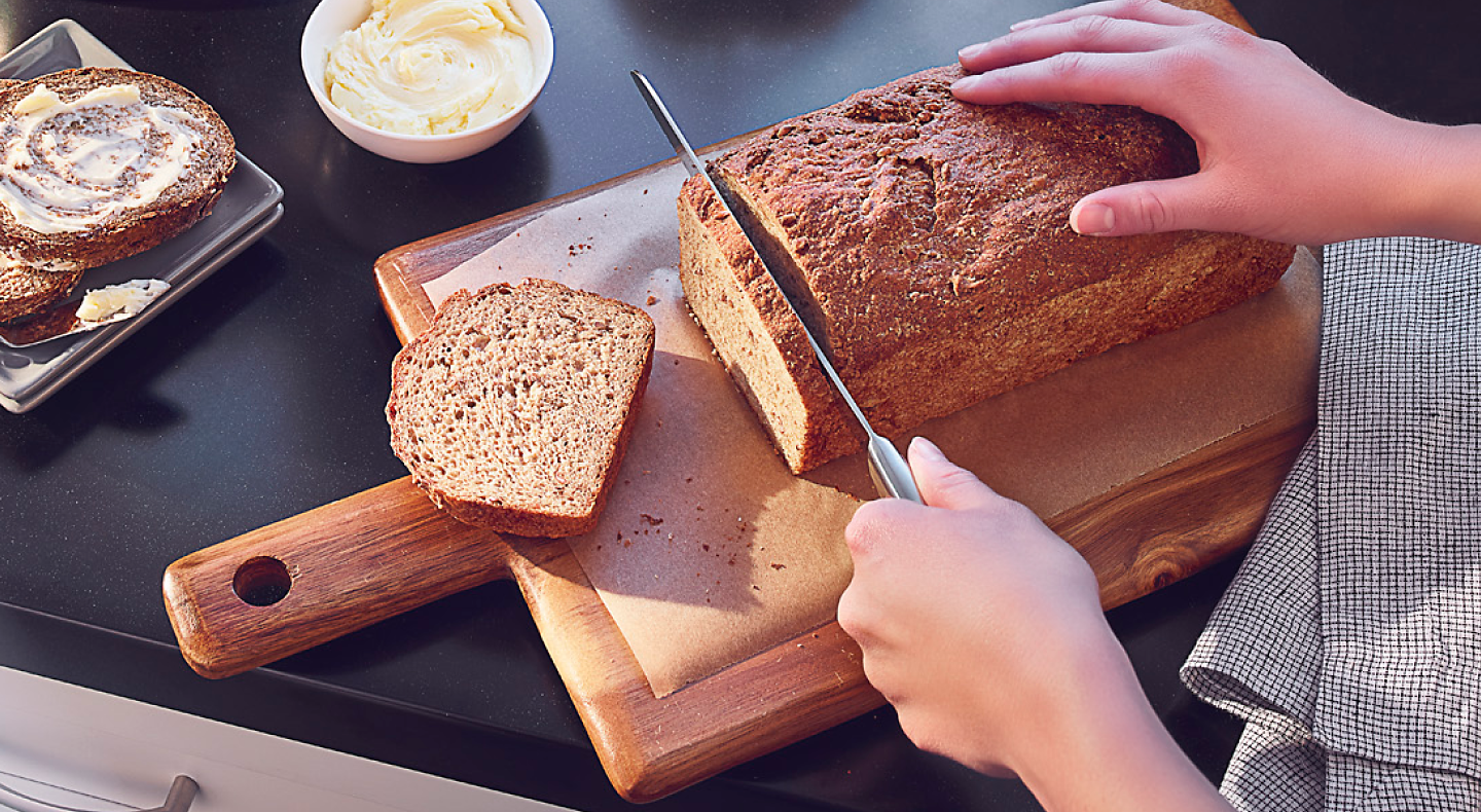 Person slicing banana bread on wooden cutting board
