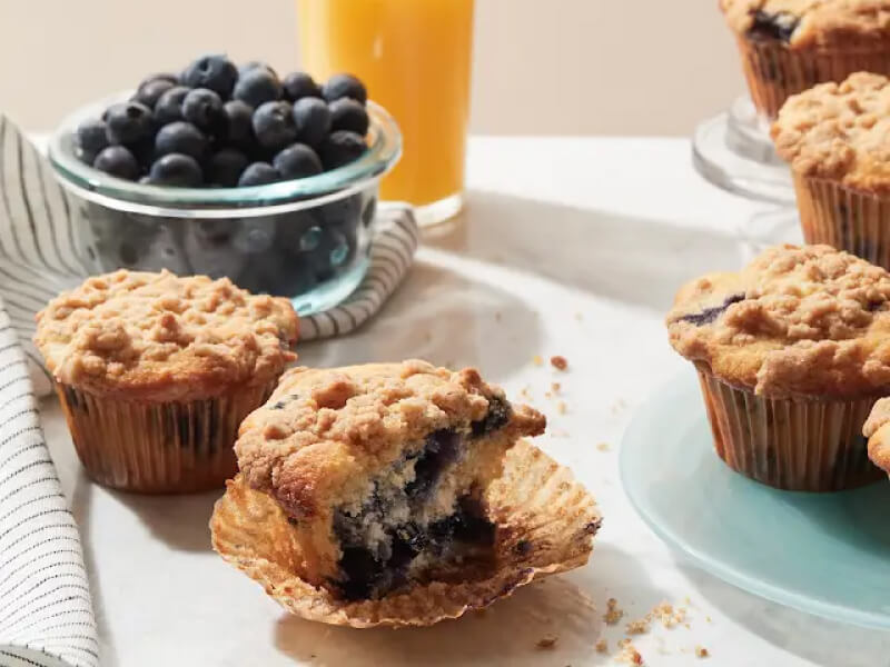 Partially eaten blueberry muffin topped with streusel inside of a muffin liner