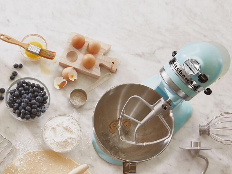 Birds-eye view of light blue stand mixer surrounded by blueberry muffin ingredients