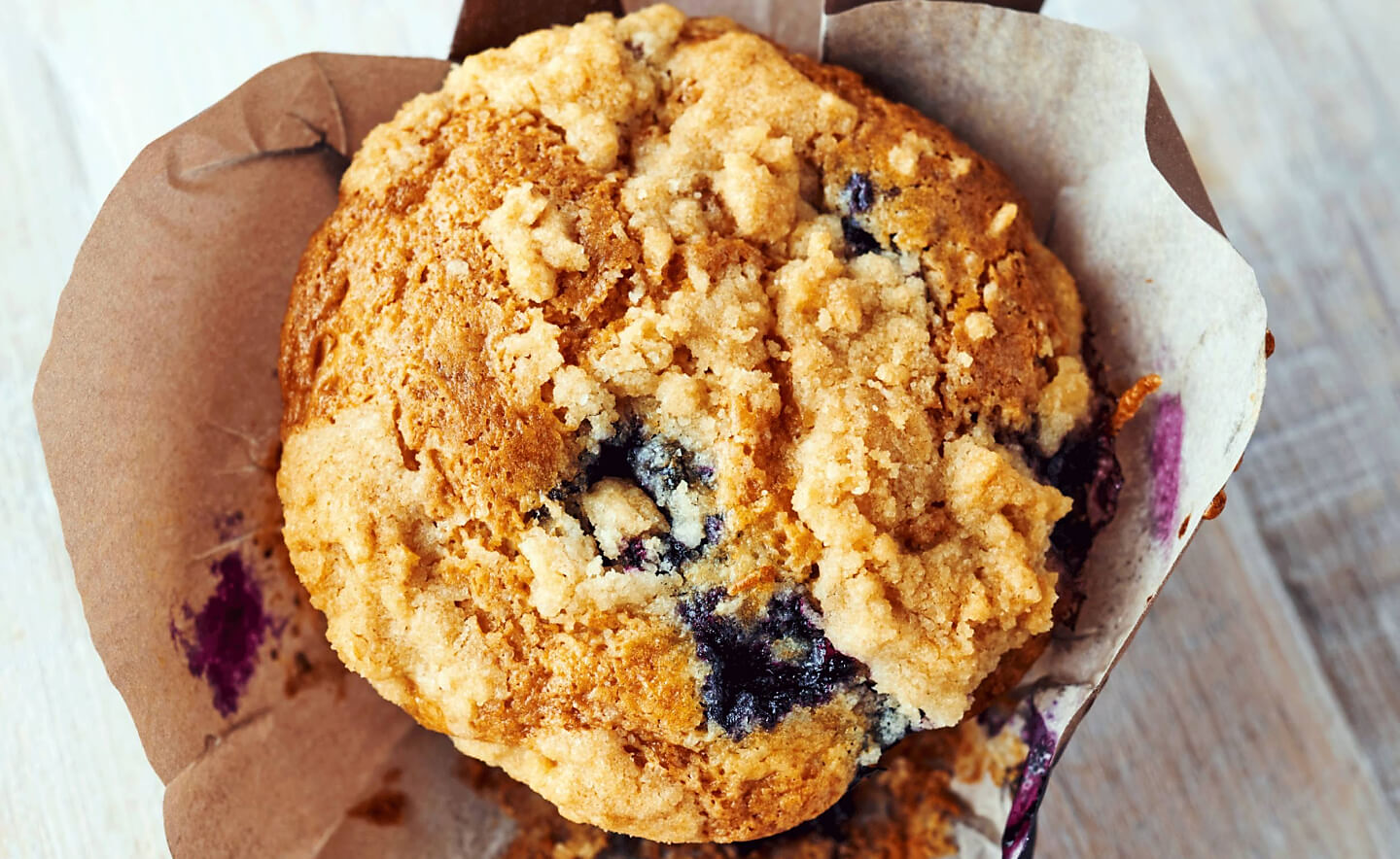 Birds-eye view of a streusel-topped blueberry muffin inside of a decorative liner