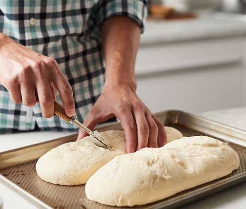 Person scoring bread dough on a baking sheet