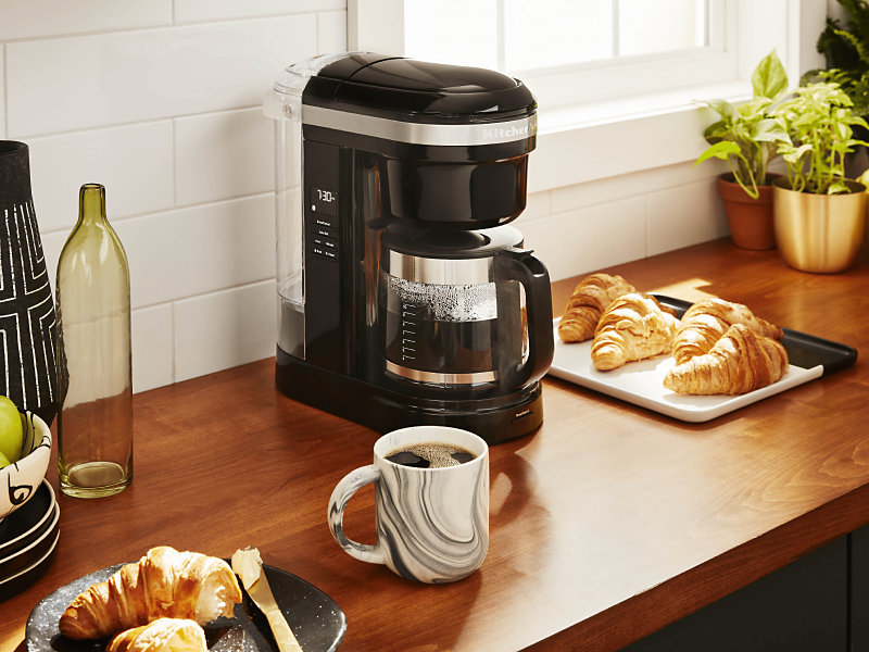 KitchenAid® coffee maker on countertop with croissants and mug of coffee