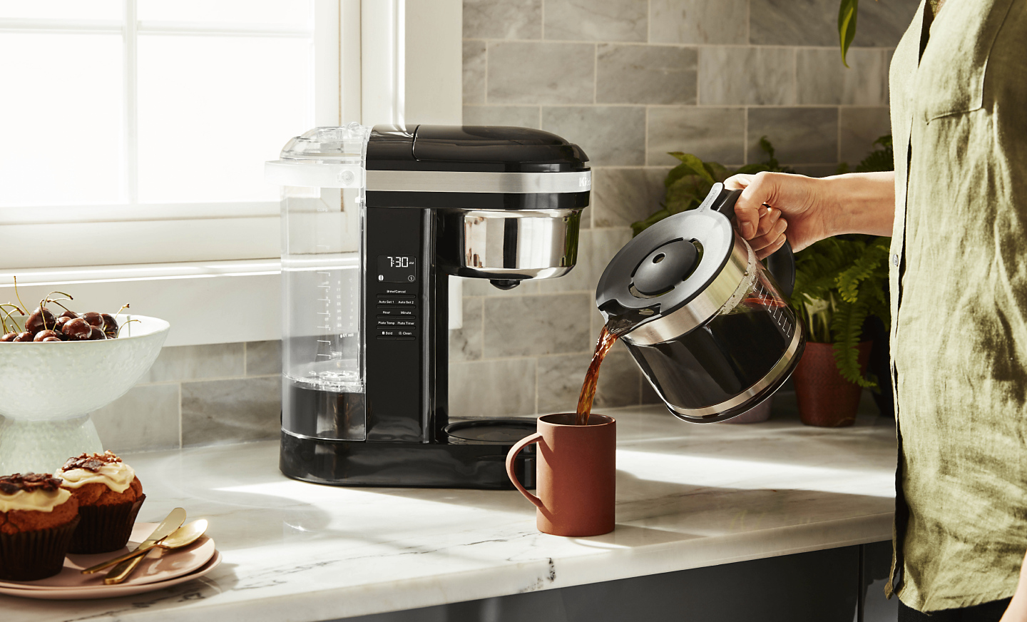 Woman pouring coffee into cup from KitchenAid® coffee maker