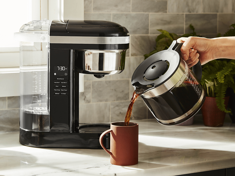 Woman pouring coffee into cup from KitchenAid® coffee maker