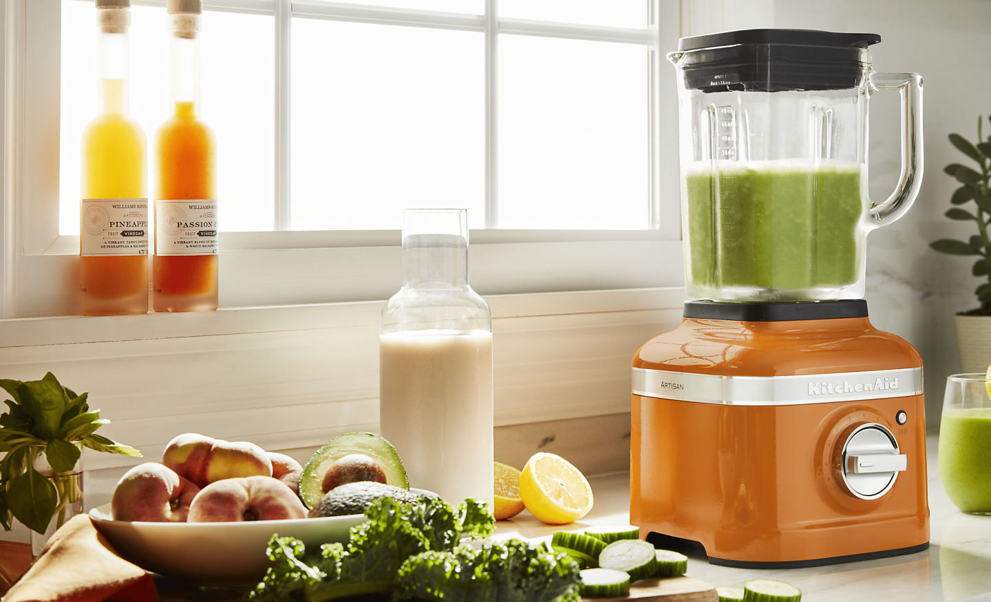 Orange KitchenAid® blender next to fresh kale