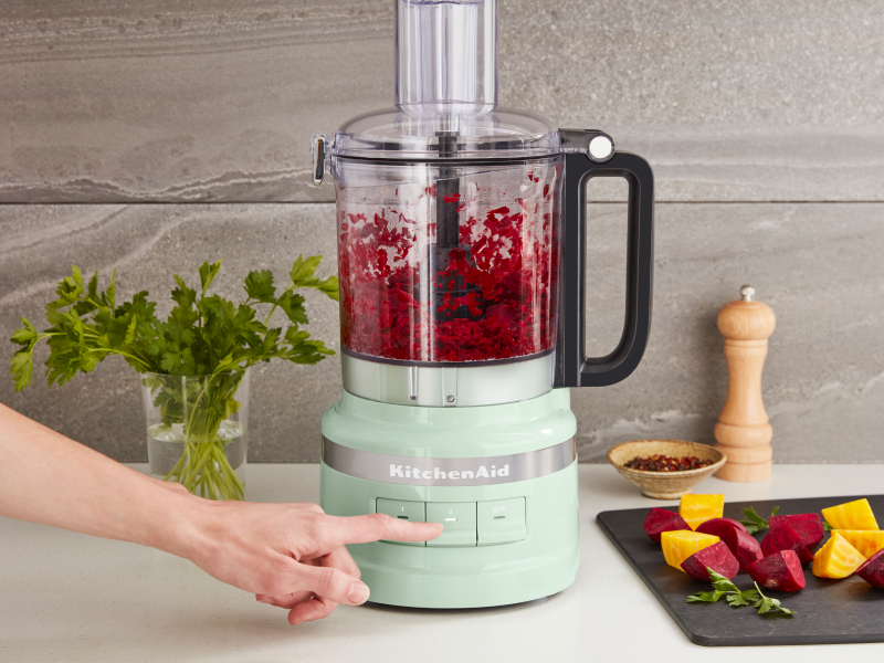 A woman chopping beets in a KitchenAid® food processor.