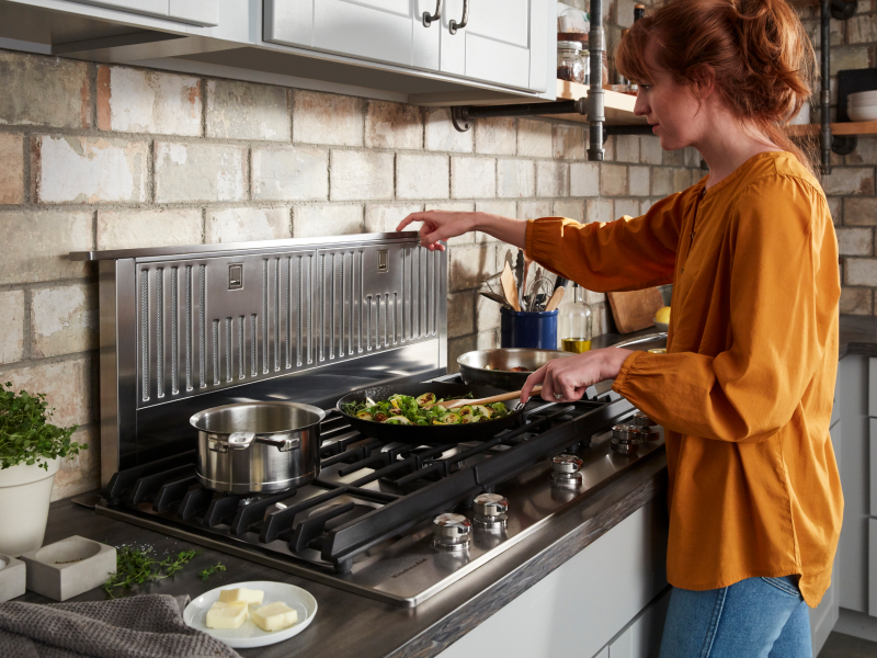 A woman stir frying vegetables on a KitchenAid® stovetop.