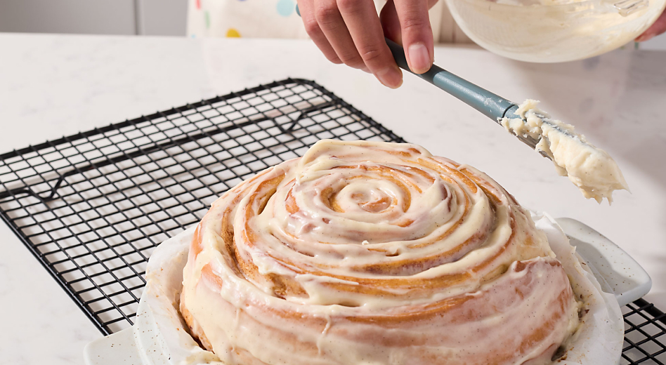 Person icing cinnamon roll bread on cooling rack