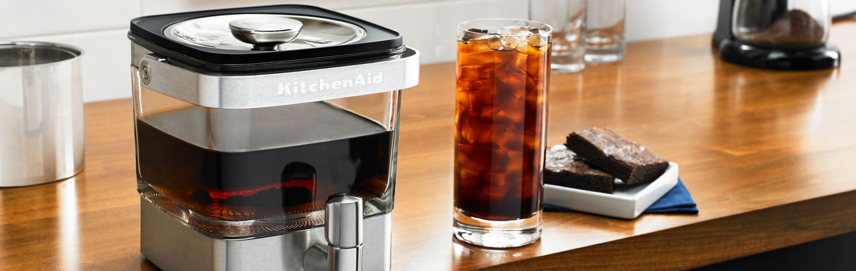 Cold brew coffee maker sitting on counter next to glass of iced coffee