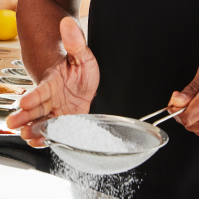 Person sifting powdered sugar with a handheld sifter