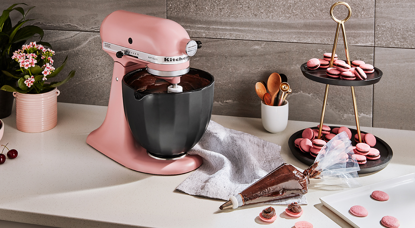 KitchenAid® stand mixer next to piping bag with chocolate buttercream frosting and macaroons