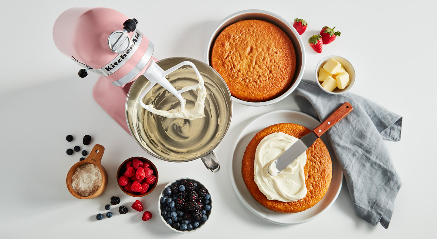 A pink KitchenAid® stand mixer with cakes and mixed berries.