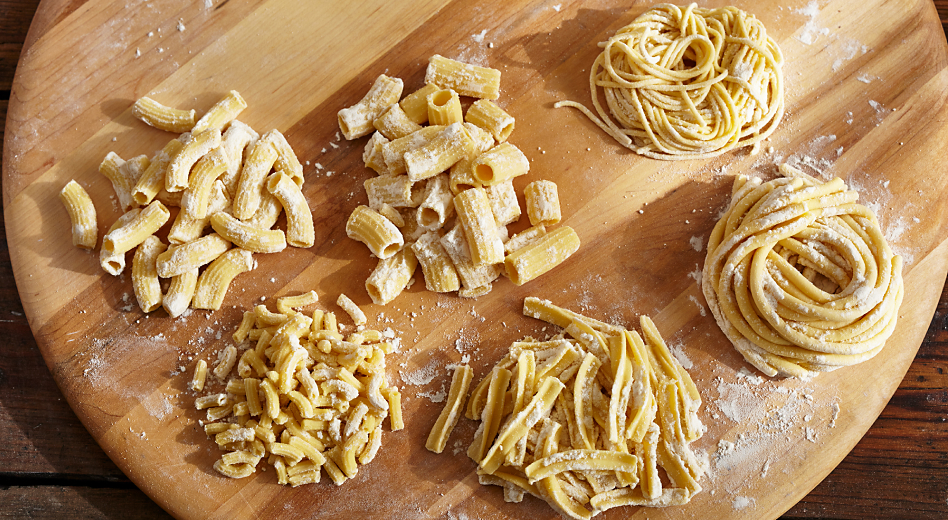 Six different types of pasta on a wooden cutting board